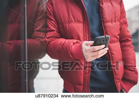 Picture - Cropped shot of young man leaning against office building reading smartphone texts. Fotosearch