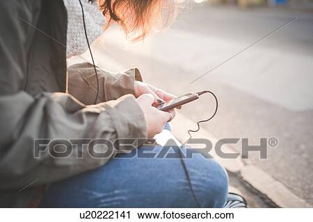 Cropped shot of young woman sitting on sidewalk reading smartphone texts View Large Photo Image Stock Image - Cropped shot of young woman sitting on sidewalk reading smartphone texts. Fotosearch