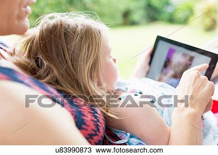 Daughter sitting on mother's lap using digital tablet View Large Photo Image Stock Image - Daughter sitting on mother's lap using digital tablet. Fotosearch