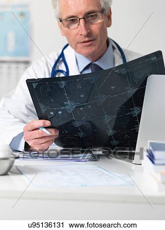 Stock Image - Doctor studying film sheet of computed tomography (CT) scans of various sections through the human head. Fotosearch
