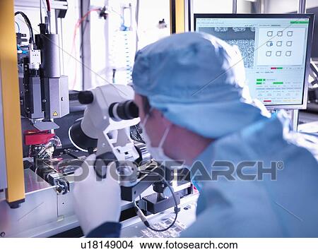 Picture - Electronics worker checking component in clean room. Fotosearch
