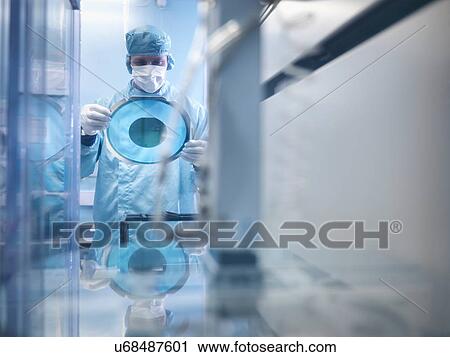 Stock Image - Electronics worker holding silicon wafer by cutting machine in clean room. Fotosearch