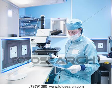 Stock Image - Electronics worker in clean room with silicon wafer. Fotosearch