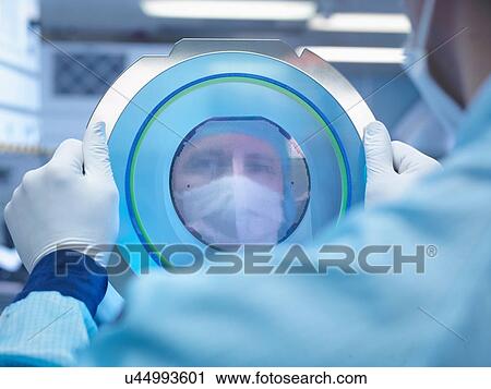 Stock Image - Electronics worker reflected in silicon wafer in clean room laboratory. Fotosearch