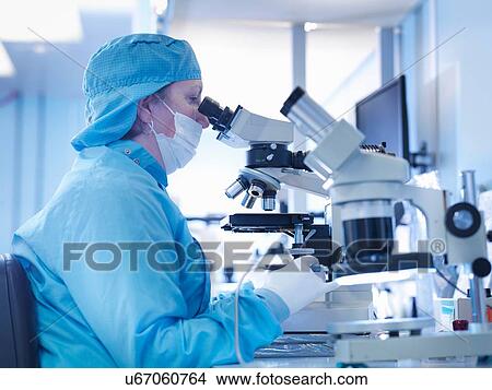 Picture - Electronics worker working with microscope in clean room. Fotosearch