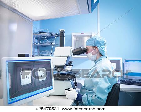 Stock Image - Electronics worker working with microscope in clean room. Fotosearch