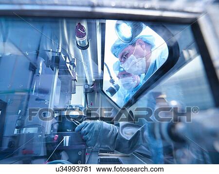 Stock Image - Electronics workers looking into sealed work station window in clean room laboratory. Fotosearch