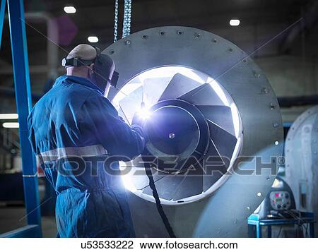 Stock Image - Engineer welding airduct part in engineering factory. Fotosearch