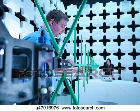 Stock Photograph - Engineers checking a bilog antenna for electromagnetic compatibility (EMC) radiated immunity testing in a semi anechoic chamber relative to the electronic equipment under test (EUT). Fotosearch