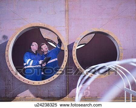 Stock Photography - Engineers inspecting large steel superstructure in engineering factory. Fotosearch