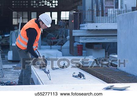 Stock Image - Factory worker attaching winch hook to concrete block in concrete reinforcement factory. Fotosearch