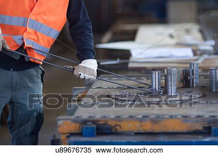 Stock Photography - Factory worker bending metal rod in concrete reinforcement factory. Fotosearch