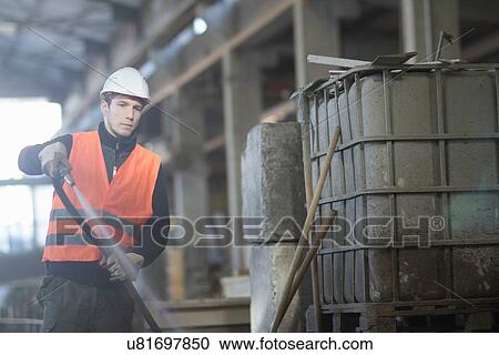 Stock Image - Factory worker cleaning up with water hose in concrete reinforcement factory. Fotosearch