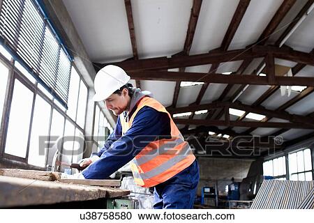 Stock Image - Factory worker hammering on workbench in concrete reinforcement factory. Fotosearch