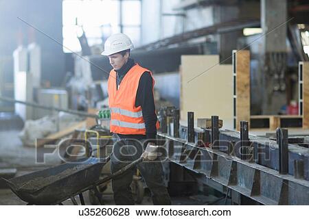 Factory worker pushing wheelbarrow in concrete reinforcement factory View Large Photo Image Stock Photo - Factory worker pushing wheelbarrow in concrete reinforcement factory. Fotosearch