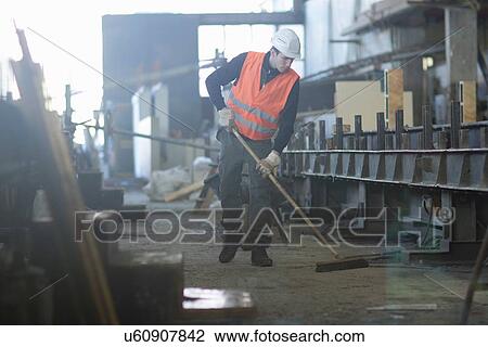 Stock Image - Factory worker sweeping up in concrete reinforcement factory. Fotosearch