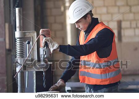 Stock Image - Factory worker using drill in concrete reinforcement factory. Fotosearch