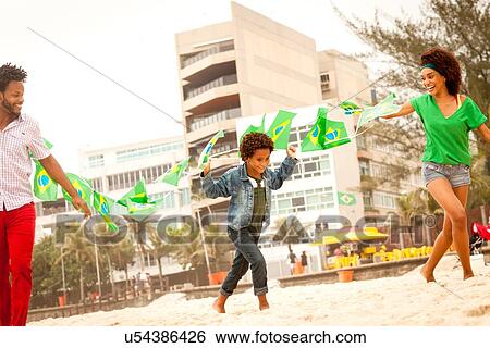 Stock Photograph - "Family playing with string of flags on beach, Rio de Janeiro, Brazil". Fotosearch