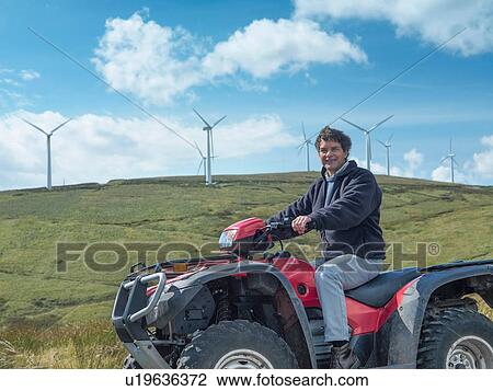 Stock Image - Farmer sitting on quadbike at windfarm. Fotosearch