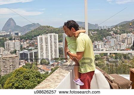 Stock Photo - "Father and daughter looking over balcony at view, Rio de Janeiro, Brazil". Fotosearch