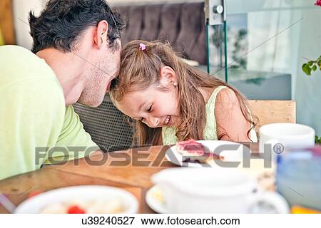 Stock Photo - "Father and daughter sitting at table together, laughing". Fotosearch