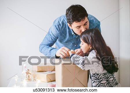 Stock Image - Father and daughter wrapping Christmas gifts. Fotosearch