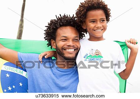 Stock Photography - "Father and son holding up Brazilian flag on Ipanema beach, Rio De Janeiro, Brazil". Fotosearch