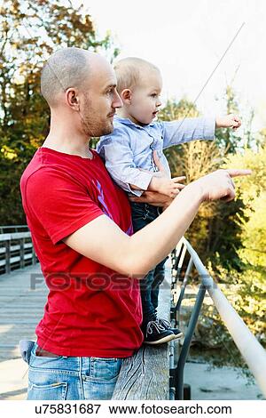 Stock Photo - "Father and son standing on bridge, looking at view, rural setting". Fotosearch