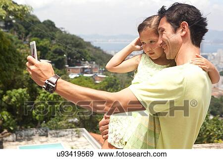 "Father holding daughter, father taking self portrait using smartphone" View Large Photo Image Stock Photo - "Father holding daughter, father taking self portrait using smartphone". Fotosearch