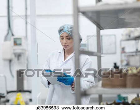 Stock Image - Female baker checking stock on digital tablet in cake factory. Fotosearch