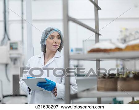 Stock Photo - Female baker checking stock on digital tablet in cake factory. Fotosearch