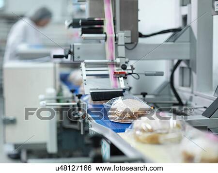 Stock Photograph - Female baker putting cakes on labelling machine in cake factory. Fotosearch