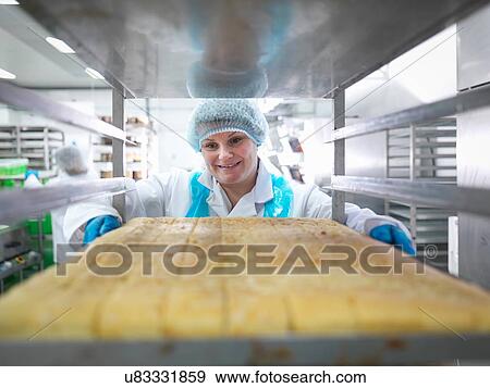 Stock Photo - Female baker with tray of cakes in cake factory. Fotosearch