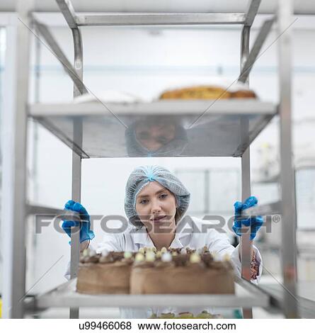 Stock Photo - Female baker with tray of fresh cakes in cake factory. Fotosearch