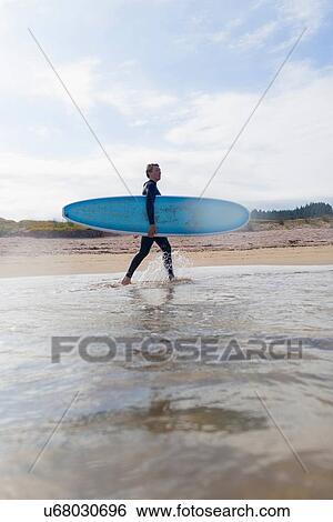 Stock Photograph - "Female surfer carrying surfboard in sea, Bay of Islands, New Zealand". Fotosearch
