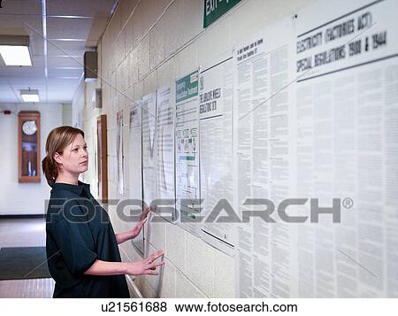 Stock Photo - Female worker looking at notice board in factory. Fotosearch
