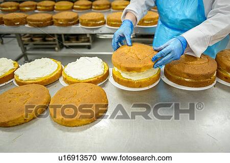 Stock Image - "Female worker places top on cake in cake factory, close up". Fotosearch