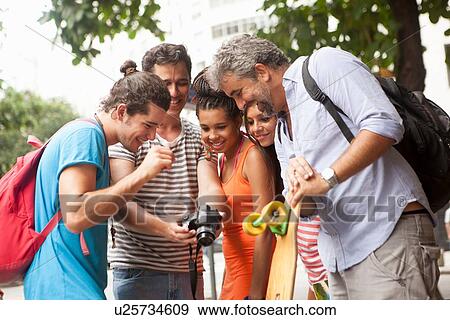 Stock Photo - "Five adult friends reviewing photos on digital camera, Copacabana town, Rio De Janeiro, Brazil". Fotosearch