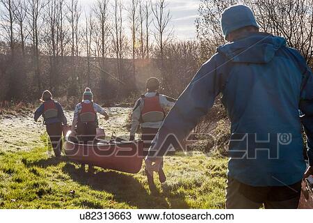Stock Image - Four people carrying canoe across grass. Fotosearch