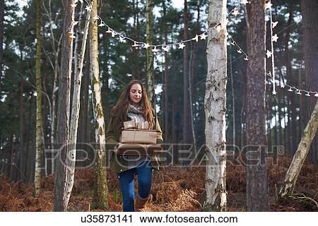 Stock Image - Gifts being carried through forest by young woman. Fotosearch