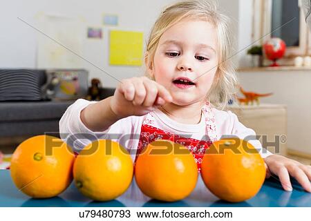 Stock Image - Girl counting oranges on table. Fotosearch