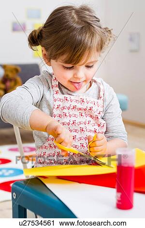 Stock Image - Girl cutting coloured card at home. Fotosearch