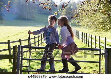 Stock Photo - Girl whispering to twin brother whilst climbing over footpath gate. Fotosearch