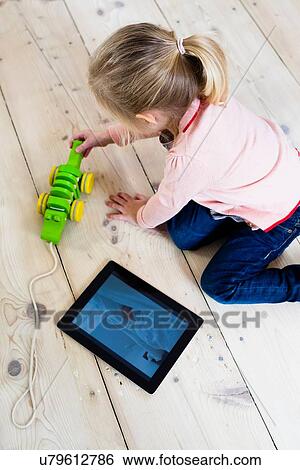 "Girl with digital tablet, playing toy on wooden floor" View Large Photo Image Stock Photograph - "Girl with digital tablet, playing toy on wooden floor". Fotosearch
