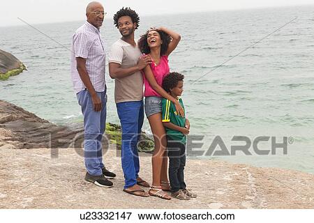 Stock Photo - "Grandfather and family standing on rock, Ipanema Beach, Rio De Janeiro, Brazil". Fotosearch