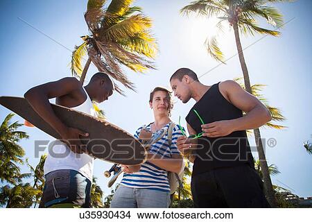 "Group of men holding skateboards, outdoors, talking, low angle view" View Large Photo Image Picture - "Group of men holding skateboards, outdoors, talking, low angle view". Fotosearch