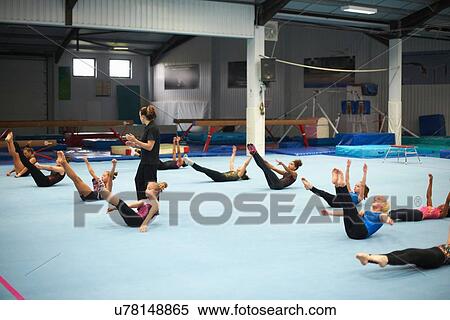 Stock Photography - Gymnastics instructor overseeing class practising stretches. Fotosearch