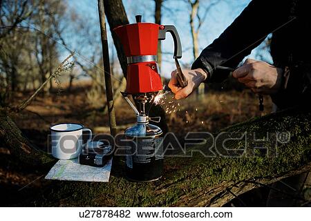 Stock Image - Hands of hiker igniting coffee pot on camping stove in woods. Fotosearch