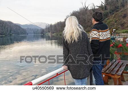 Stock Photo - "Heterosexual couple standing beside lake, Lombardy, Italy, rear view". Fotosearch