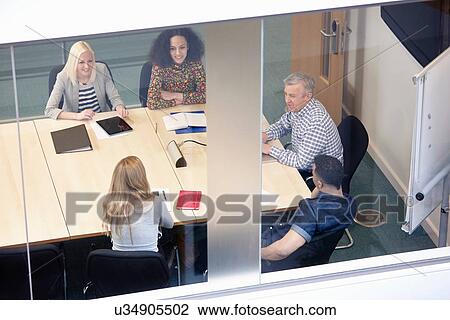 Stock Image - High angle view of businessmen and women having meeting at conference table. Fotosearch
